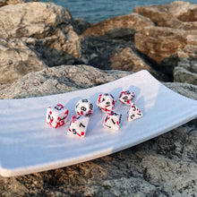 Load image into Gallery viewer, Bloody Aftermath Dice Set Boasting a morbid spray of red on a clean ivory face, these dice suggest tales of heroism, survival, and violence. When your character is packing an edge that draws blood, how better to lean into the fun that to wear it on your dice? These dice are made for your assassin, vampire, werewolf, or blood magic wielder. Inked in black as a dark backstory, these dice are fun for almost any horror roleplaying games.