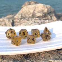 Load image into Gallery viewer, Treasure Glow Dice Set These dice, infused with a faint glitter and flakes of gold leaf, give off the aura of a treasure pile freshly plundered. The black inking offers a confident and no-fuss legibility that gets you efficiently from the initiative roll to the coin-counting. These dice are perfect for characters with a taste for the finer things in life - your rogues, bards, mercenaries, and the odd King in Yellow.
